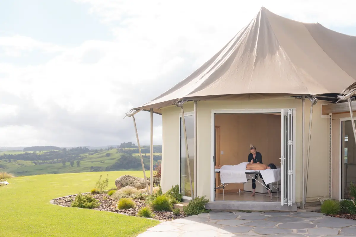 Family flying a kite on the hilltop lawn at Pōhutukawa Tent, glamping Waitomo