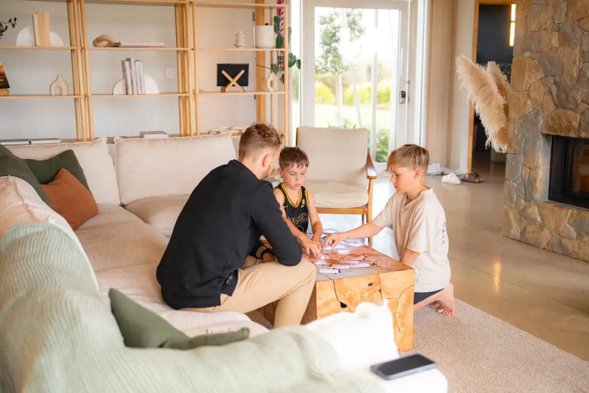 Pōhutukawa Tent family in lounge playing card games by the stone fireplace, NZ