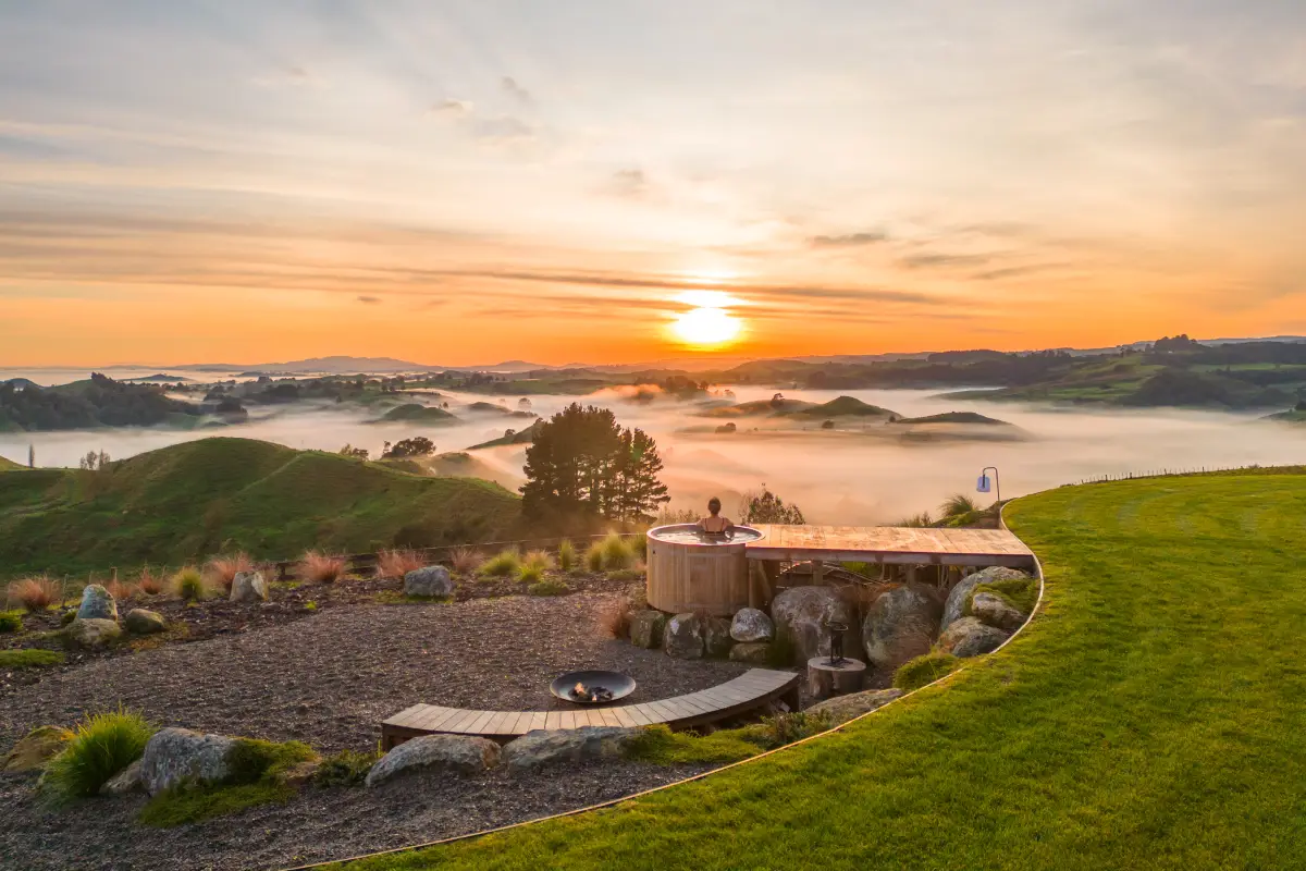 Pōhutukawa Tent hot tub at sunrise with fog over rolling hills, luxury glamping NZ