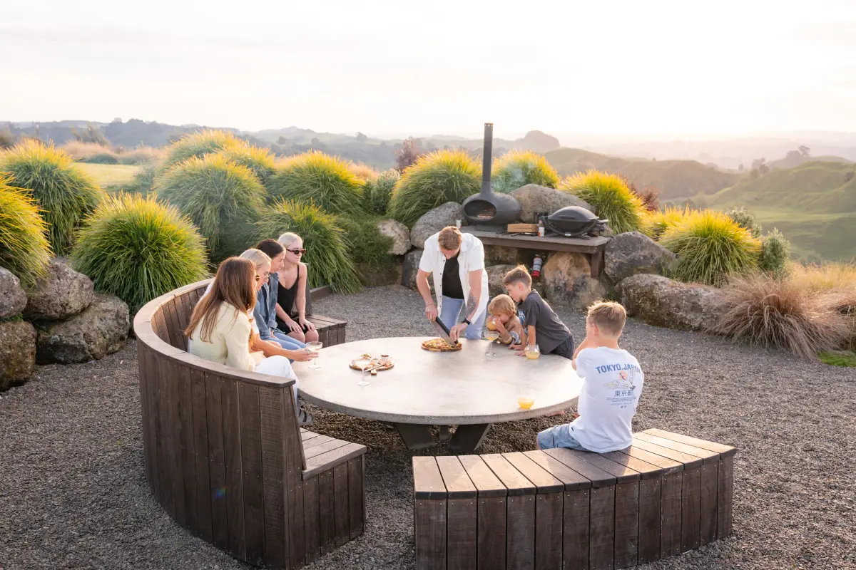 Group dining outdoors at sunset at Pōhutukawa Tent, Waitomo glamping